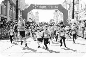 The children begin to run the Nova Post race. Smiling adults run alongside them and cheer them on.